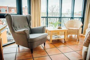 A room with a grey armchair, a wicker chair, and a small wooden table with a vase of flowers. - Tower House Holiday Apartment 10 (Kühlungsborn)