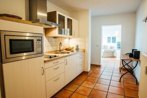 Una cocina moderna con armarios blancos, microondas integrado y piso de baldosas.
