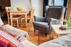 Ein Zimmer mit grauem Sessel, einem Holzespeisetisch, Stühlen und einem kleinen Tisch mit einer Pflanze.