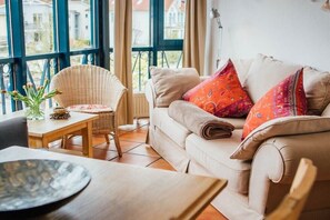Ein gemütliches Wohnzimmer mit einer Couch, einem Sessel, einem Tisch und einem Fenster mit Blick auf Gebäude.