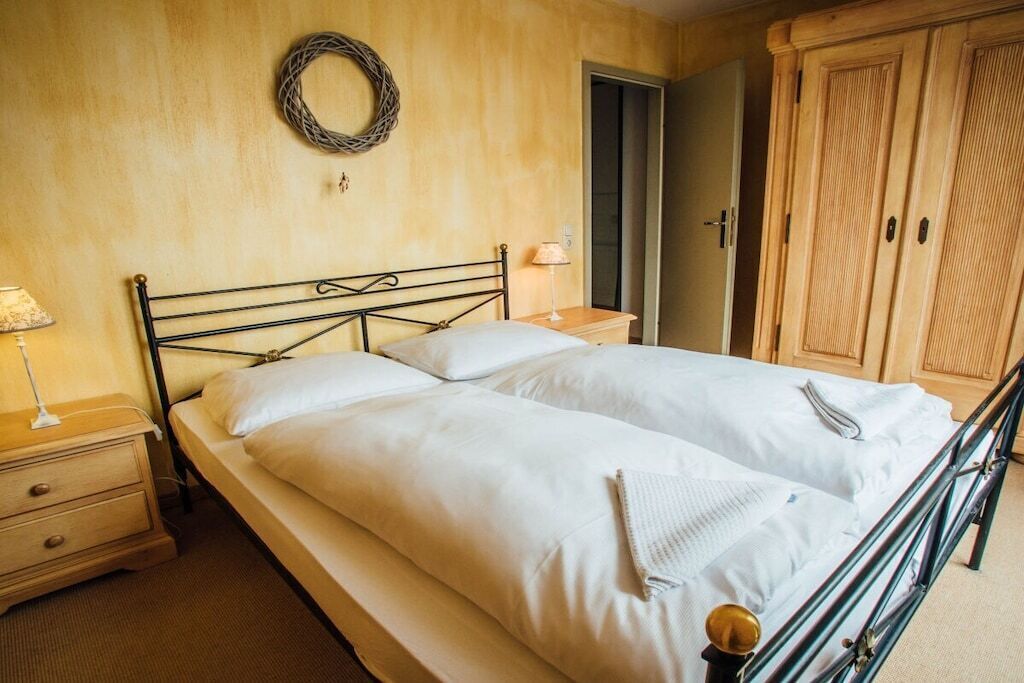 A double bed with a metal frame, a bedside table with a lamp, a wooden wardrobe, and a door leading to another room.