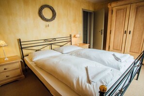 Una cama doble con estructura metálica, una mesita de noche con lámpara, un armario de madera y una puerta que da a otra habitación.
