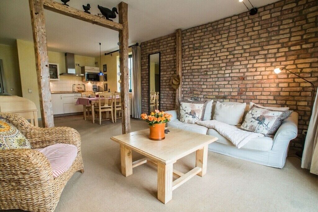 Een gezellige woonkamer met een bakstenen muur, een witte bank, een rieten stoel en een houten salontafel met bloemen.