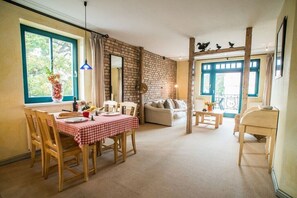 Ein gemütliches Wohnzimmer mit Backsteinwand, einem Essbereich mit kariertem Tischlein und einem Balkon mit Blick.