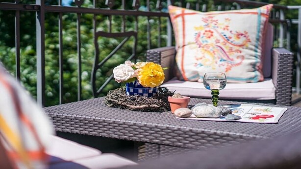 Área de estar ao ar livre em vime, com almofada, um pequeno vaso com flores, um copo d'água e um papel com um desenho.