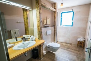 Un baño con tocador de madera, un lavamanos blanco, inodoro y un taburete pequeño.