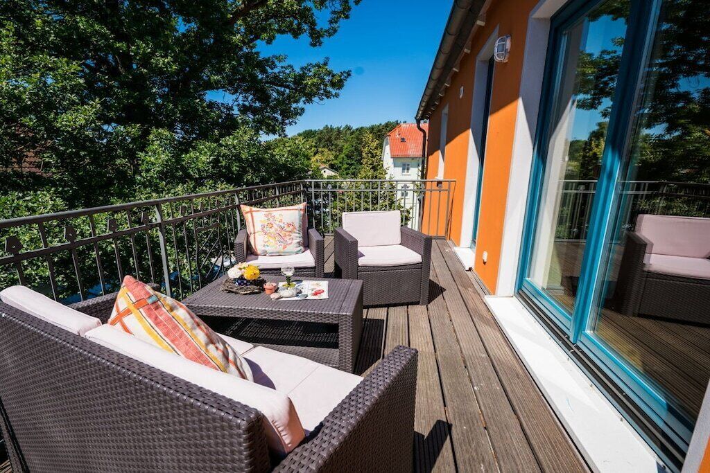 A balcony with wicker furniture, a table with items, and a glass door leading to a building.