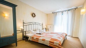Quarto com cama, penteadeira, espelho, luminária na parede e janela com cortinas.