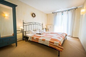 Un dormitorio con cama, cómoda, espejo, luz empotrada en la pared y ventana con cortinas.