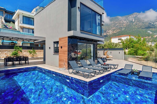 A modern two-story building with a swimming pool, outdoor seating, and a mountain view. - Walk Distance to the Town (Kaş)