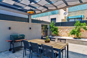 An outdoor patio with a wooden table and chairs, a grill, and potted plants. - Walk Distance to the Town (Kaş)