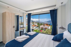 A modern hotel room with a large bed, a wooden wardrobe, a bathroom, and a balcony with a city view. - Walk Distance to the Town (Kaş)