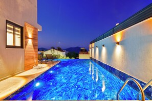 A swimming pool with a blue tint, a wooden deck, and a chair. - Walk Distance to the Town (Kaş)