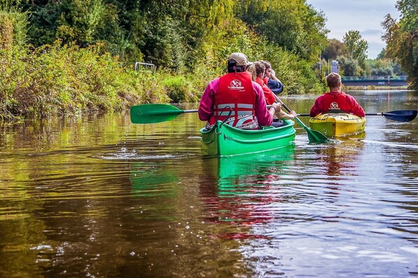 A group of people in a green boat on a calm river, surrounded by lush greenery.