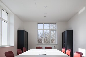 A conference room with a long table, six chairs, two black cabinets, and a large window with a view of trees.
