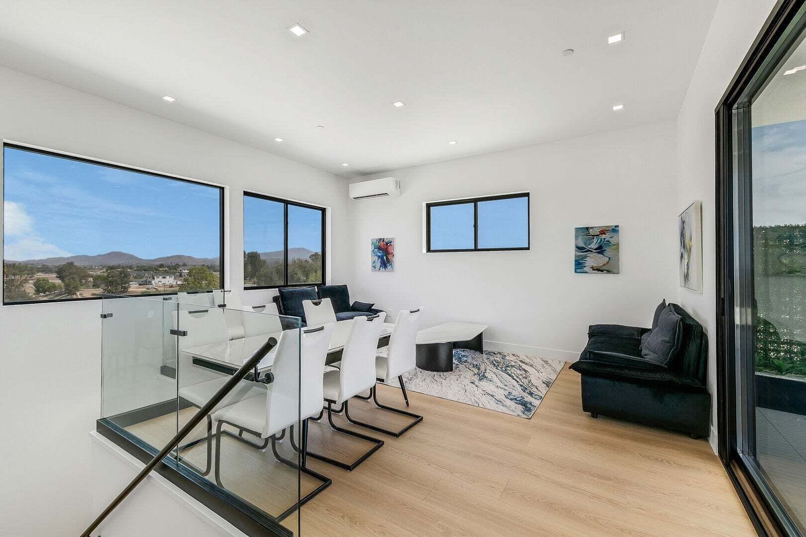 A modern interior with a glass table, white chairs, a black sofa, and artwork on the walls.