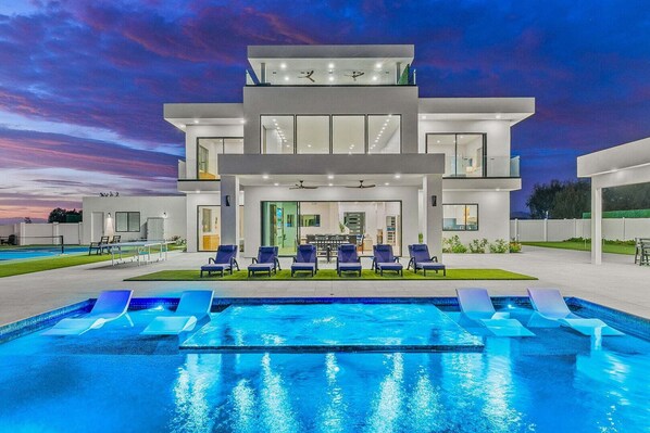 Una casa moderna de dos pisos con piscina y sillones de descanso.
