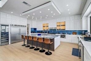 A modern kitchen with a central island, stainless steel appliances, and a blue backsplash. - Villa Spectacular - Luxury Hilltop Estate | Wine Country Views (Temecula)