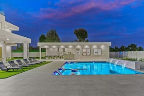 Un espace piscine extérieur moderne, doté de chaises longues, d’un bar et d’un espace salon abrité.