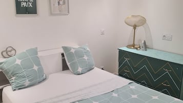 Et soveværelse med seng, puder, et kommode, en lampe og to billeder hængende på væggen.