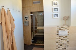 A bathroom with a glass shower enclosure, a towel rack with towels, a wall-mounted light fixture, and a decorative item. - Holiday home in Zingst with sauna (Zingst)
