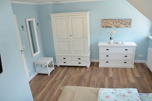 A bedroom with a large wardrobe, a bedside table, a dresser, and a bed with a floral bedspread. - Holiday home in Zingst with sauna (Zingst)