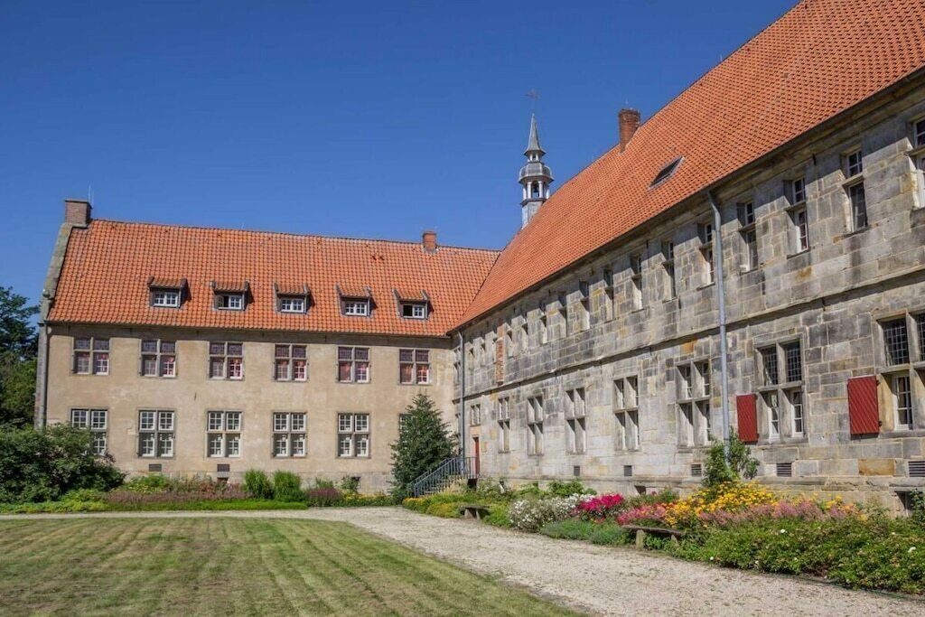 Un edificio histórico con tejado de tejas rojas y muros de piedra, que presenta una fachada simétrica con ventanas regularmente distribuidas y una entrada central.
