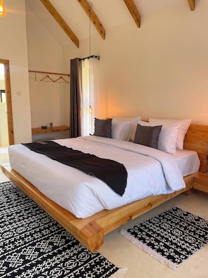Cama com estrutura de madeira, roupa de cama branca e manta preta.