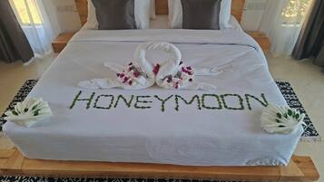 Una cama impecablemente arreglada con una toalla y flores dispuestas para deletrear 'HONEYMOON' sobre el edredón.