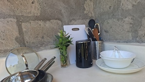 Un plan de travail de cuisine avec des ustensiles de cuisine, une planche à découper, une plante et des couverts.