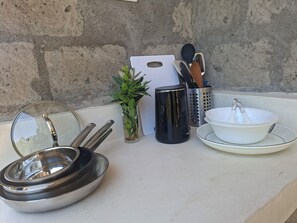 A kitchen counter with cookware, a cutting board, a plant, and utensils.