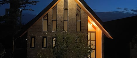 A modern house with a sloped roof, large windows, and a well-lit entrance.