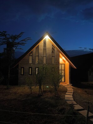 A modern house with a sloped roof, large windows, and a well-lit entrance.