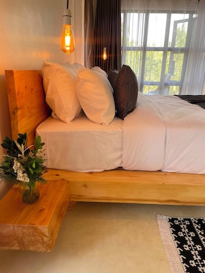 Cama com roupa de cama branca, cabeceira de madeira e um vaso com folhagem.