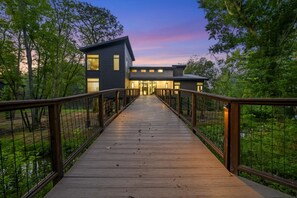 A modern building with a wooden deck leading to a gated entrance, surrounded by trees. - The Treehouse River + Secluded + High Luxe (Eagletown)