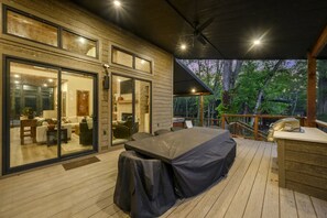 A covered outdoor deck with a dining table and chairs, a barbecue grill, and a view of trees. - The Treehouse River + Secluded + High Luxe (Eagletown)