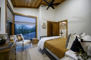 A bedroom with a bed, bedside table, chair, and a view of the outdoors through a large window. - The Treehouse River + Secluded + High Luxe (Eagletown)