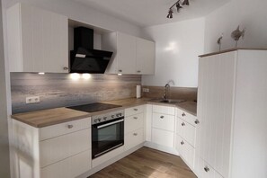 A modern kitchen with white cabinetry, a wooden countertop, a built-in oven, and a black range hood. - Holiday home with 1 bedroom (Wangerland)