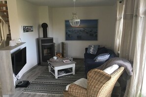 A living room with a fireplace, a sofa, a coffee table, and a painting on the wall. - Holiday home with 3 bedrooms (Nienhagen)