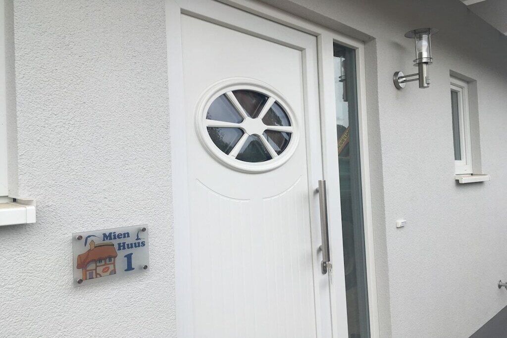 Eine weiße Tür mit rundem Fenster, Klingel und einem Schild mit der Aufschrift 'Mien Huis 1'.