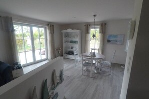 A room with a dining table, chairs, a white cabinet, and a window with curtains. - Holiday home with 3 bedrooms (Nienhagen)