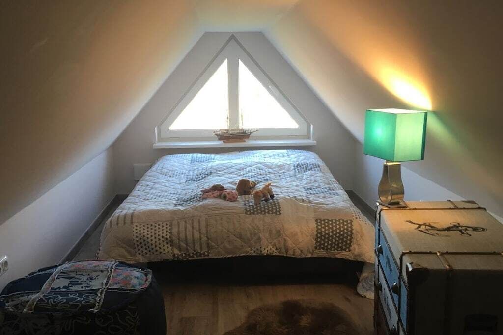 A bedroom with a sloped ceiling, a bed with a quilt, a nightstand with a lamp, and a window with a view.