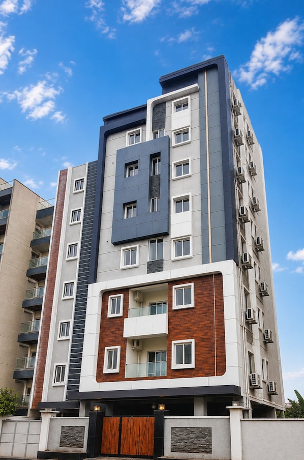 A multi-story residential building with a modern architectural design, featuring a combination of brick and concrete facades, and a prominent central entrance with a wooden door. - Hotel Sun Shine Classic (Hyderabad)