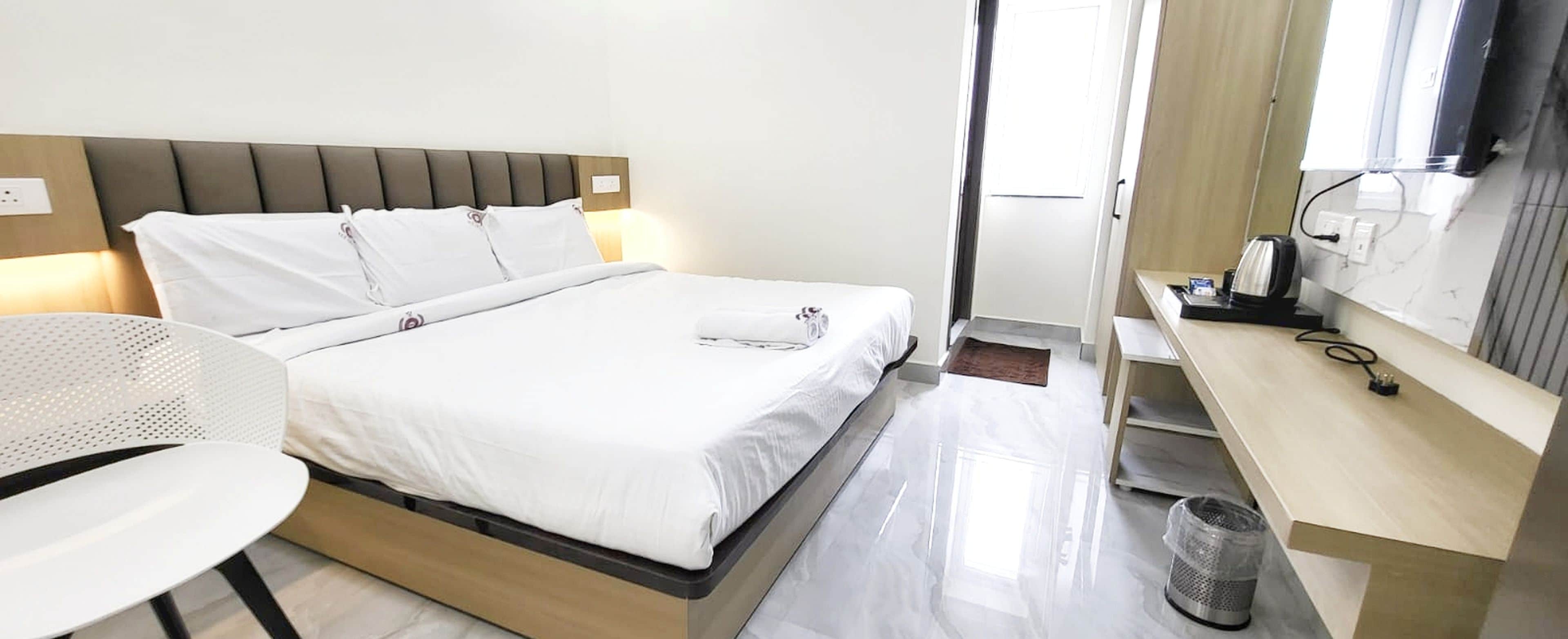 Habitación de hotel con cama, mesita de noche, silla y vistas al exterior.