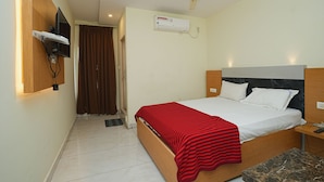 Ein Hotelzimmer mit einem Bett, einem Deckenventilator, einer Klimaanlage, einem an der Wand montierten Fernseher und einem kleinen Tisch mit Fernbedienung.