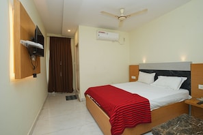 Een hotelkamer met een bed, een plafondventilator, een airconditioningapparaat, een aan de muur bevestigde televisie en een tafeltje met een afstandsbediening.