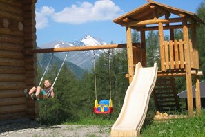 A wooden play structure with a slide and swings, set against a mountainous backdrop. - Holiday apartment with 2 bedrooms (Heiligenblut)