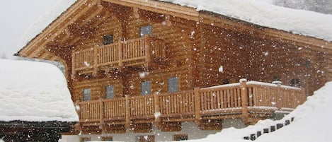 A wooden cabin with a balcony, surrounded by snow.