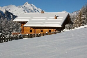 A wooden cabin with a sloped roof, surrounded by snow-covered mountains and trees. - Holiday apartment with 2 bedrooms (Heiligenblut)