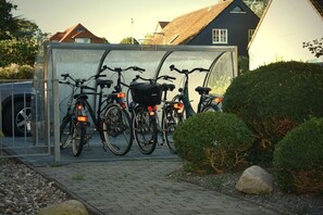 A sheltered bicycle parking area with three bicycles, a clear pathway, and a hedge. - at the sailing school (Heiligenhafen)